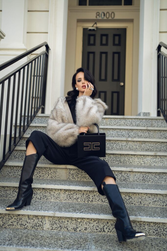 Mujer con abrigo de piel y bolso de lujo sentada en una escalinata, imagen de estilo asociada al visual merchandising en moda